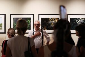 il fotografo Valter Bernardeschi durante la presentazione della mostra, di spalle alla parete con 4 sue foto incorniciate si rivolge al pubblico ripreso di spalle