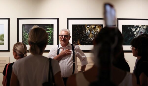 il fotografo Valter Bernardeschi durante la presentazione della mostra, di spalle alla parete con 4 sue foto incorniciate si rivolge al pubblico ripreso di spalle