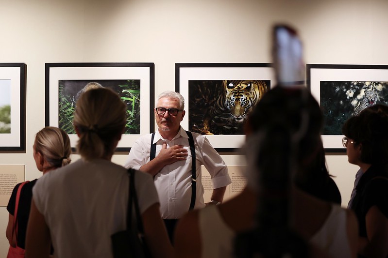 il fotografo Valter Bernardeschi durante la presentazione della mostra, di spalle alla parete con 4 sue foto incorniciate si rivolge al pubblico ripreso di spalle