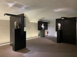 visione trasversale di una sala del museo, tre teche nere contenenti ciascuna un busto di marmo